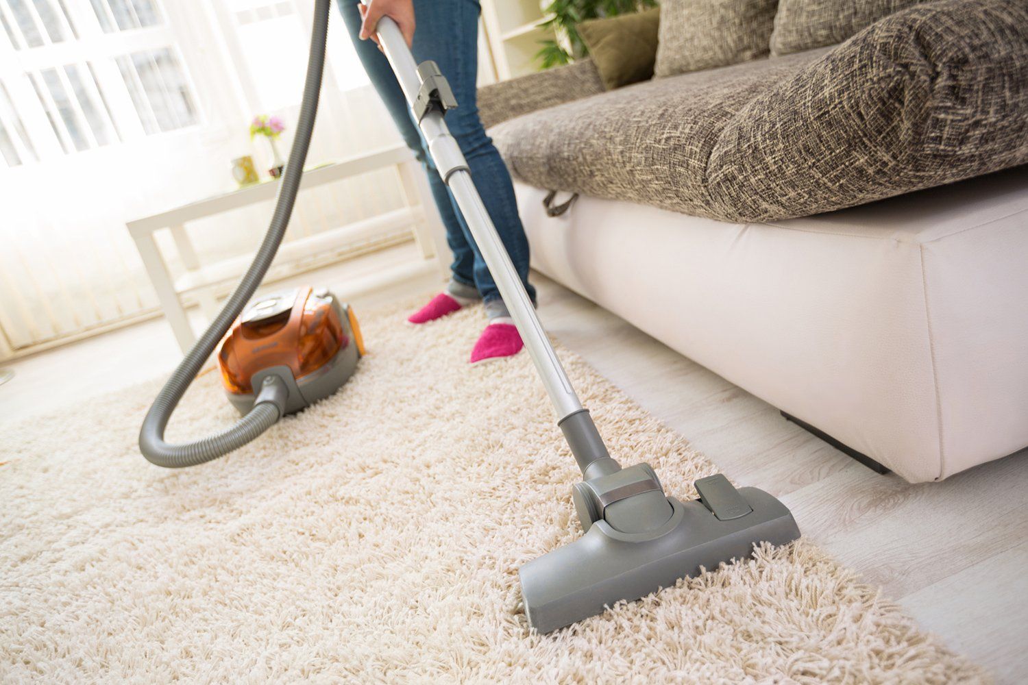 Vacuum cleaner on a white carpet beside a sofa in a bright living room