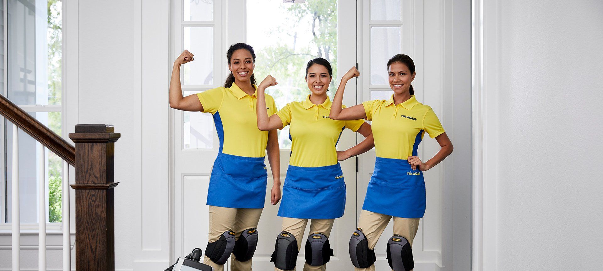 Three people in yellow shirts and blue skirts pose indoors, one flexing an arm and another holding a hand to the hip