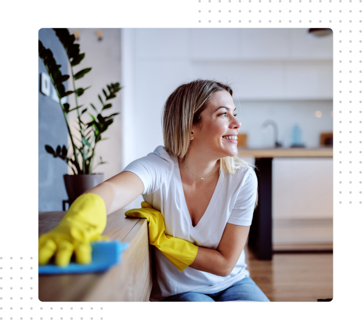 Person in yellow gloves cleaning a sofa, smiling in a bright kitchen.