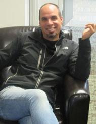 Smiling man in a black jacket sitting on a leather chair with one hand raised