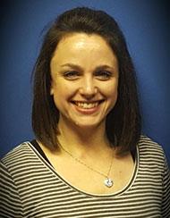 Smiling person with shoulder-length dark hair wearing a striped top against a blue background