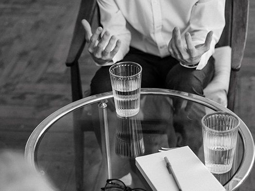 A man is sitting at a table with two glasses of water and a notebook.