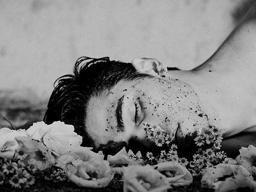 A black and white photo of a man laying on the ground with flowers on his face.