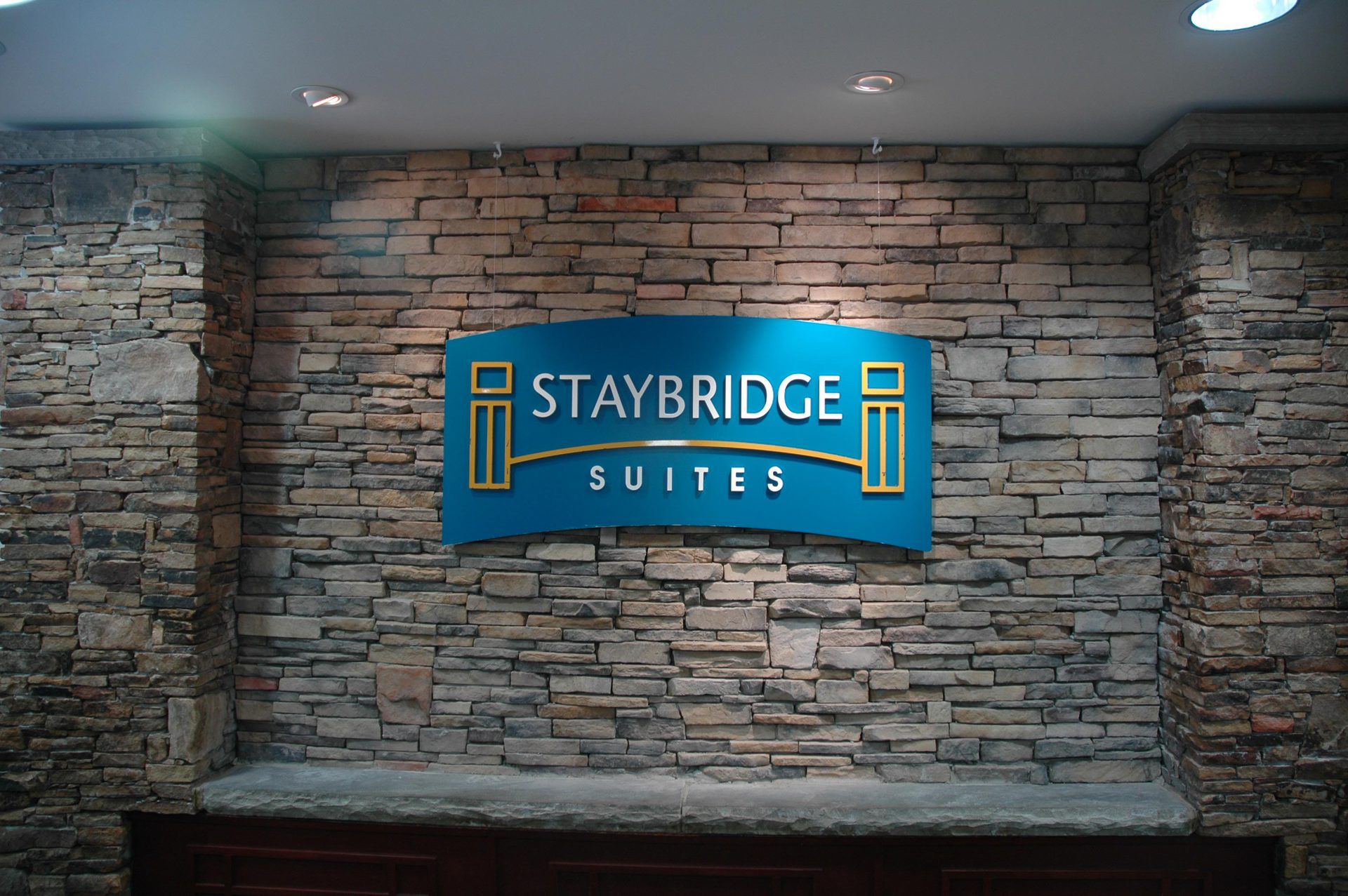 A blue sign on a stone wall says staybridge suites