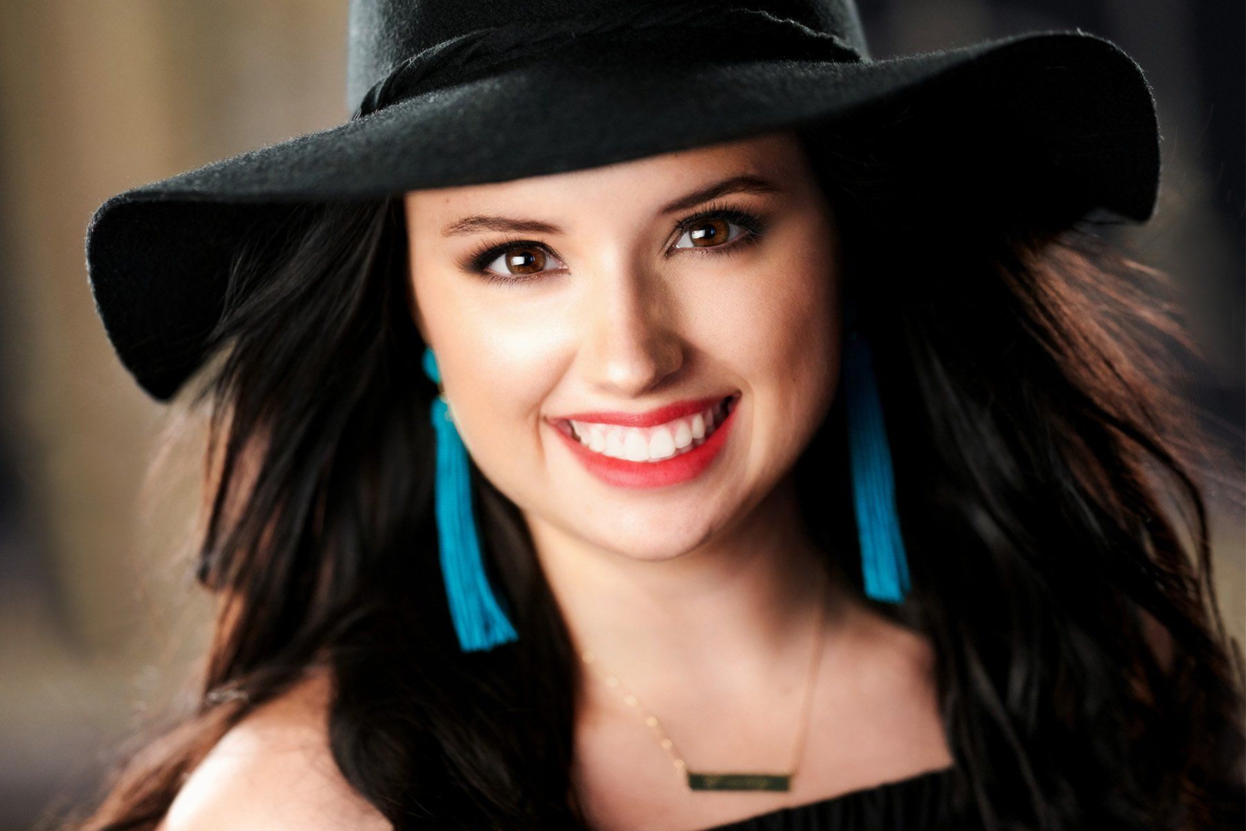 A woman wearing a black hat and blue earrings is smiling.