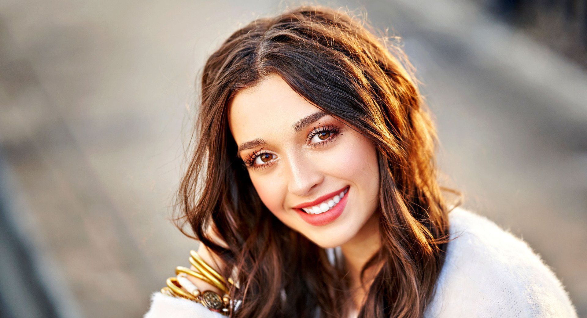 A woman with long hair is smiling and wearing a fur coat.