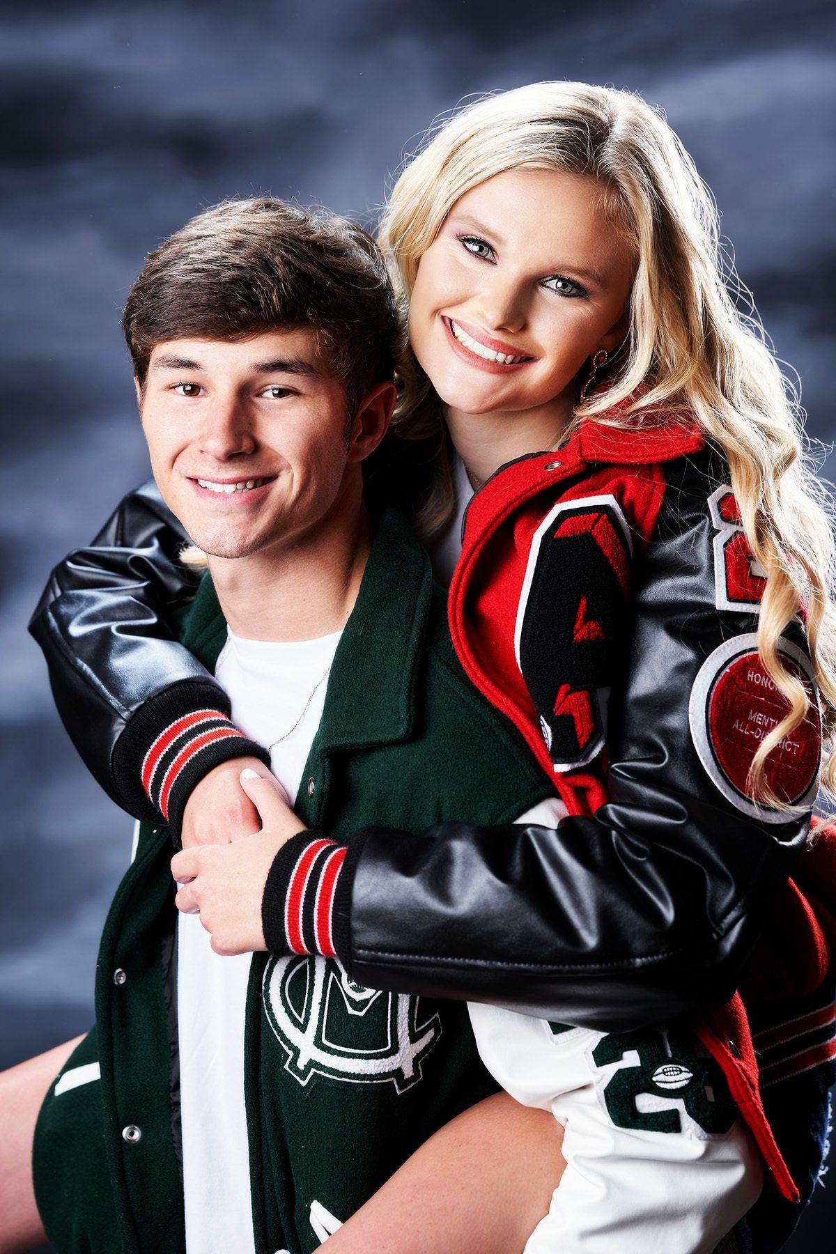 A man is carrying a woman on his back and they are wearing letterman jackets.
