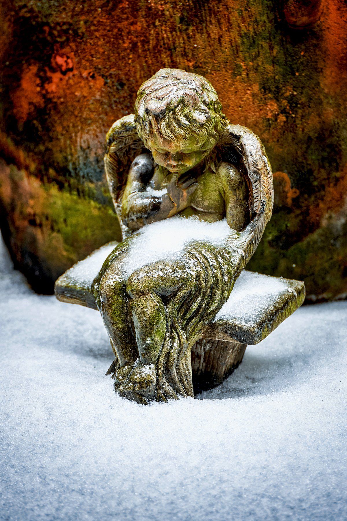 A statue of an angel sitting on a bench in the snow.