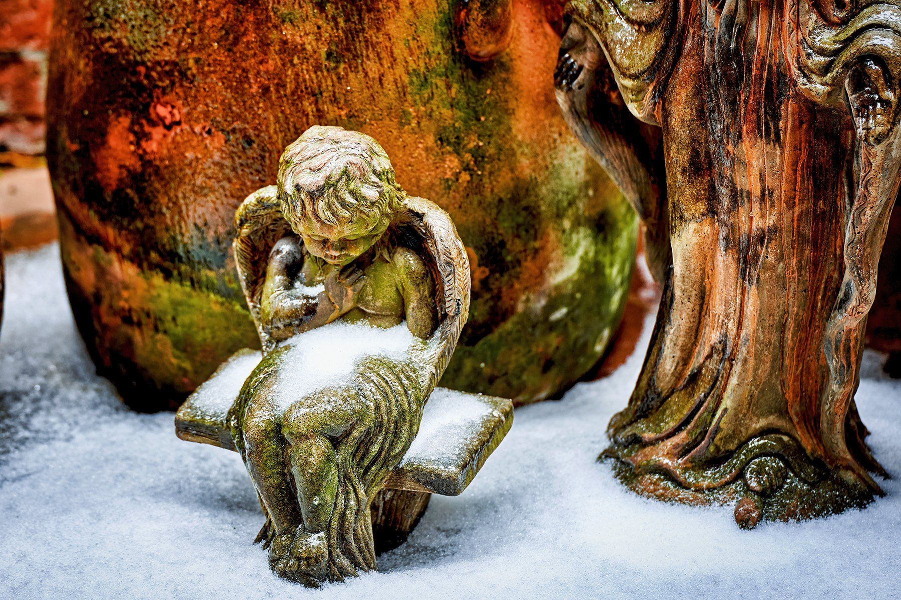 A statue of an angel is sitting on a bench in the snow.