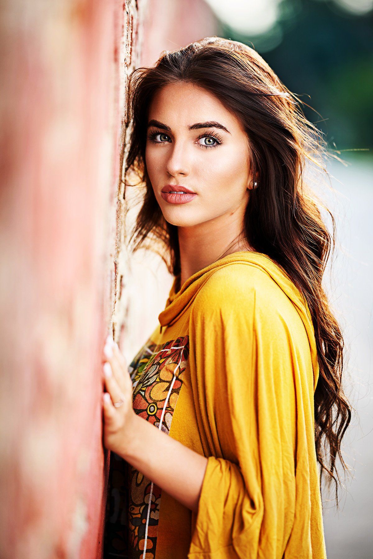A woman in a yellow dress is leaning against a wall.