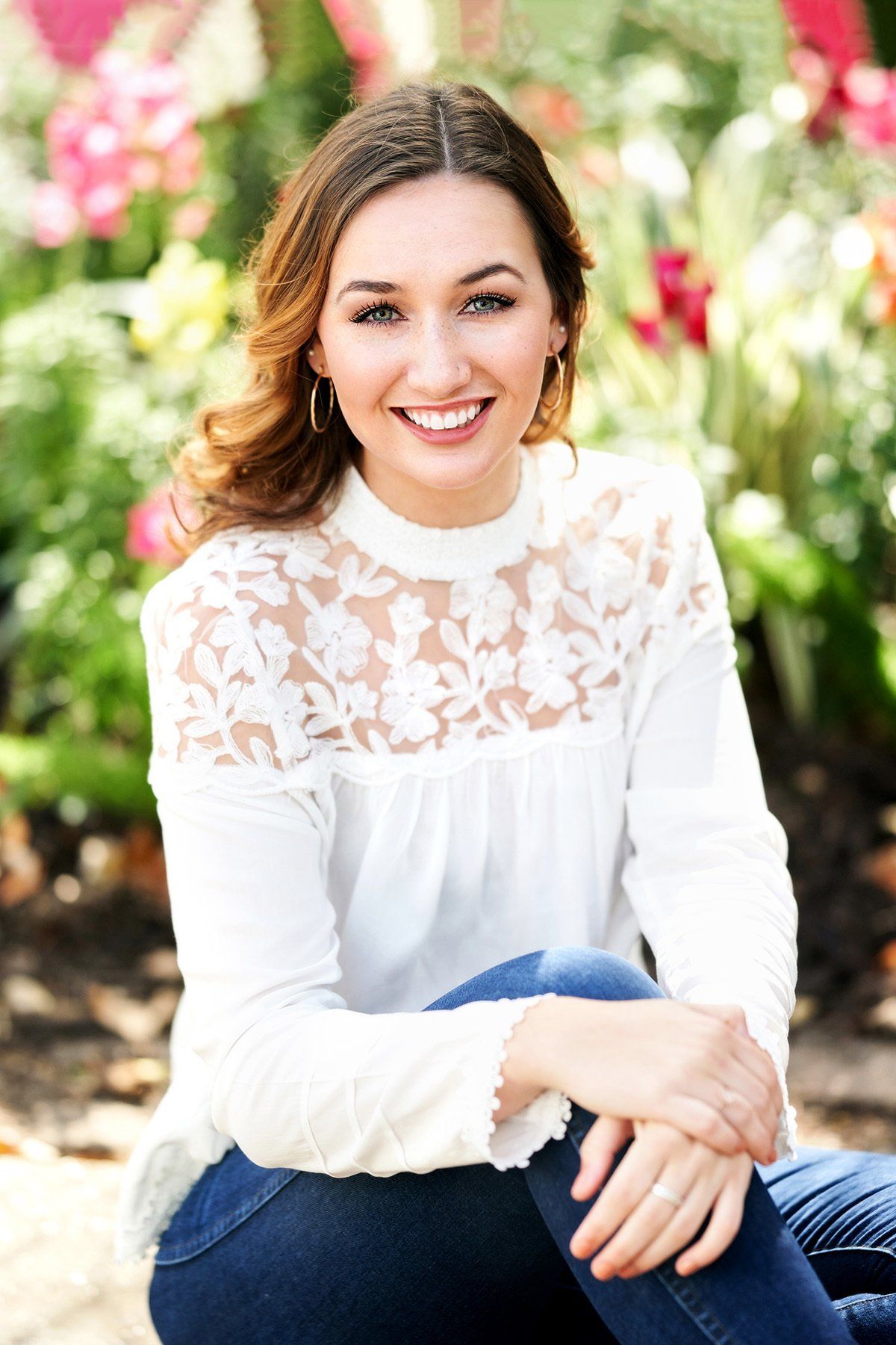 A woman in a white lace top is sitting in front of flowers.