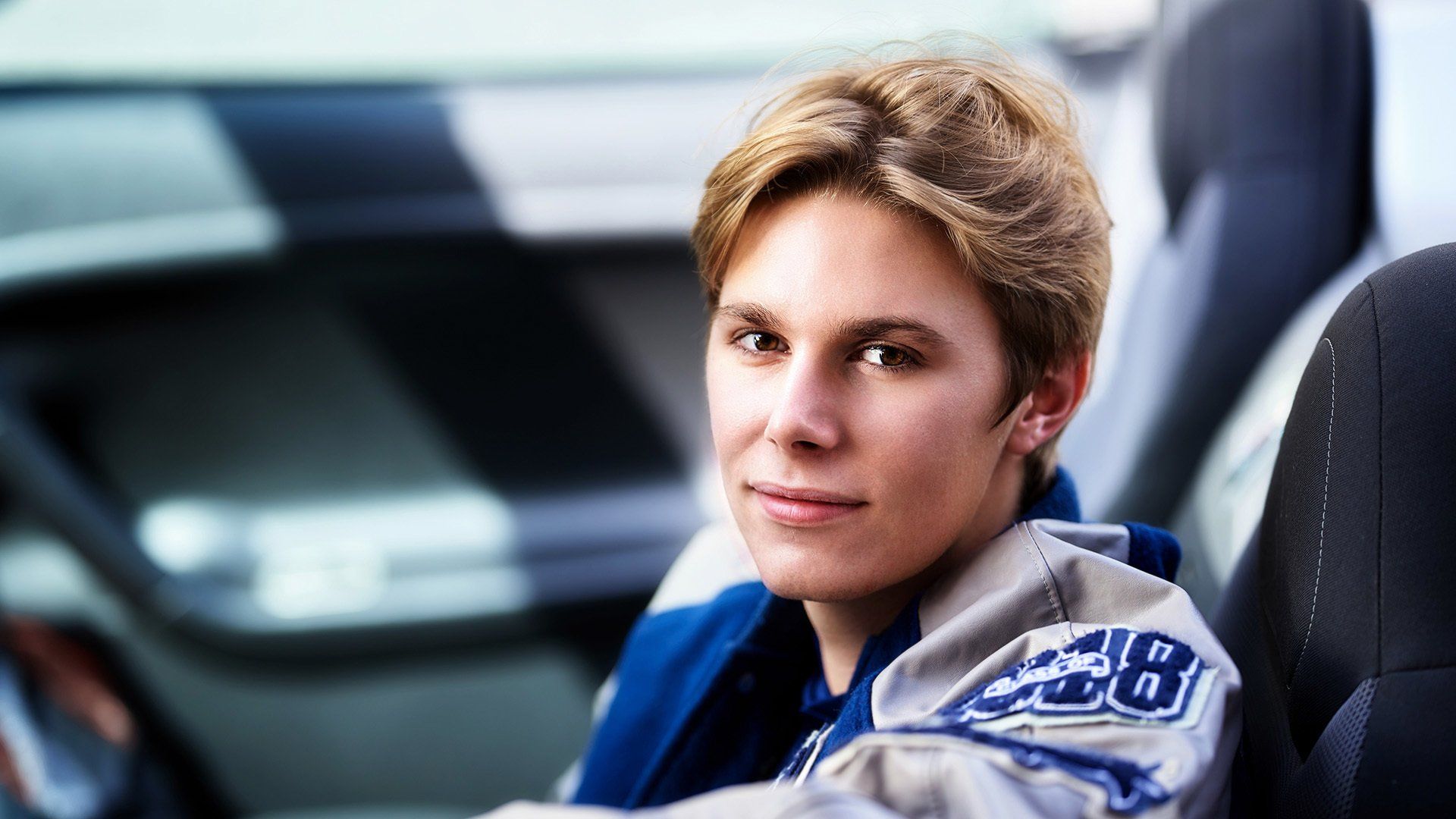 A young man is sitting in the driver 's seat of a car.