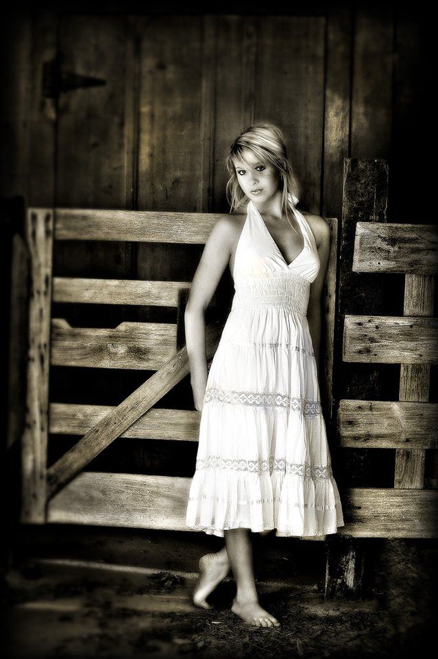 A woman in a white dress is standing in front of a wooden gate