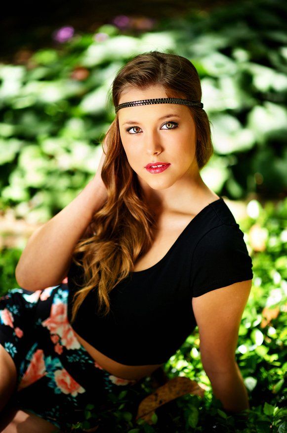 A woman in a black top and floral skirt is sitting in the grass.