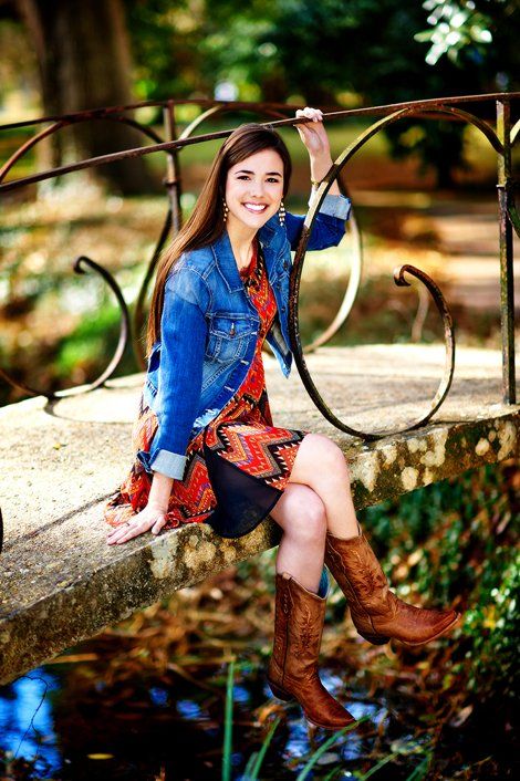 A woman in a dress and cowboy boots is sitting on a bridge.
