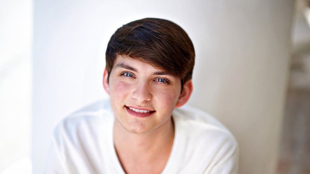 A young man in a white shirt is smiling and looking at the camera.
