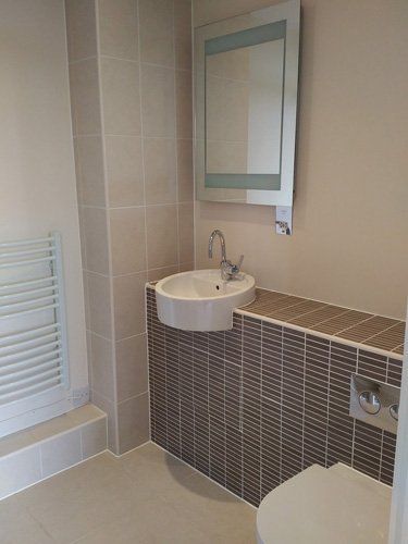 Sink in clean bathroom in corner under wall mirror with toilet just in view