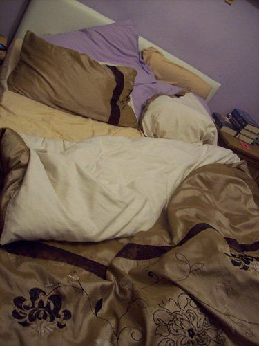 Unmade bed with books on bedside cabinet