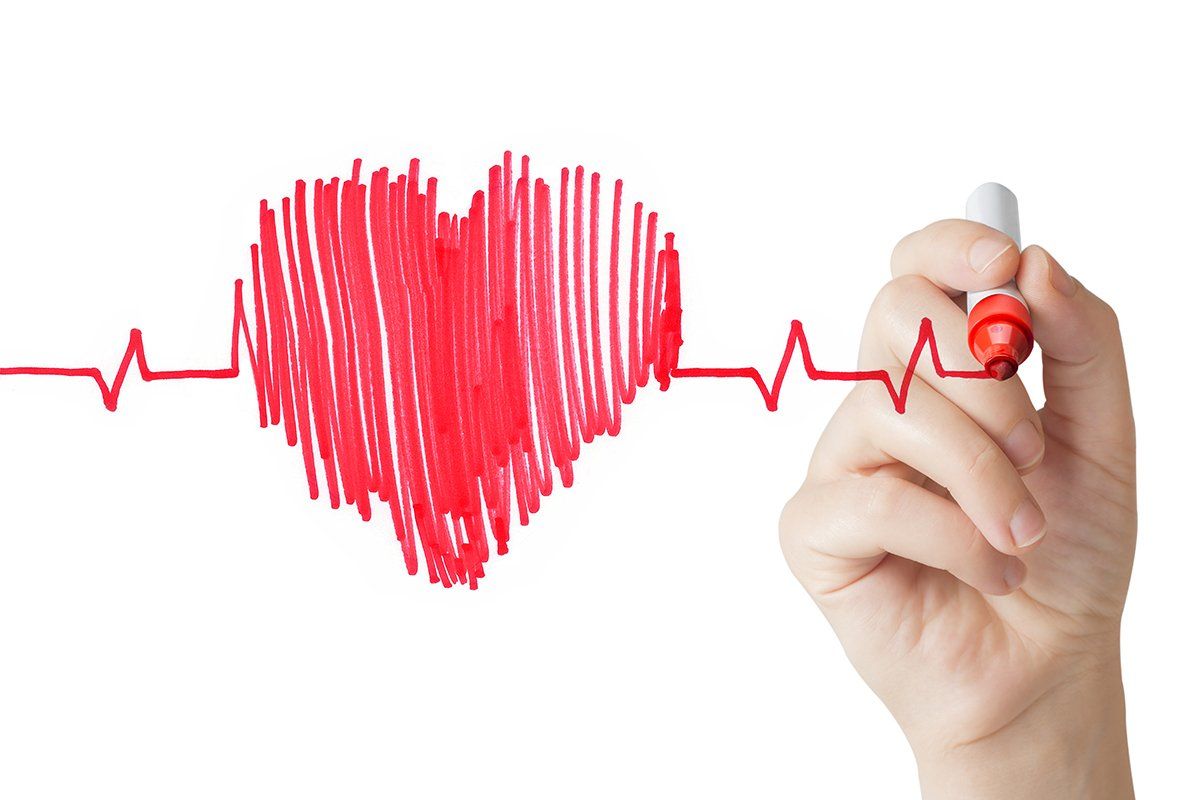A hand is drawing a heart with a marker on a white board.