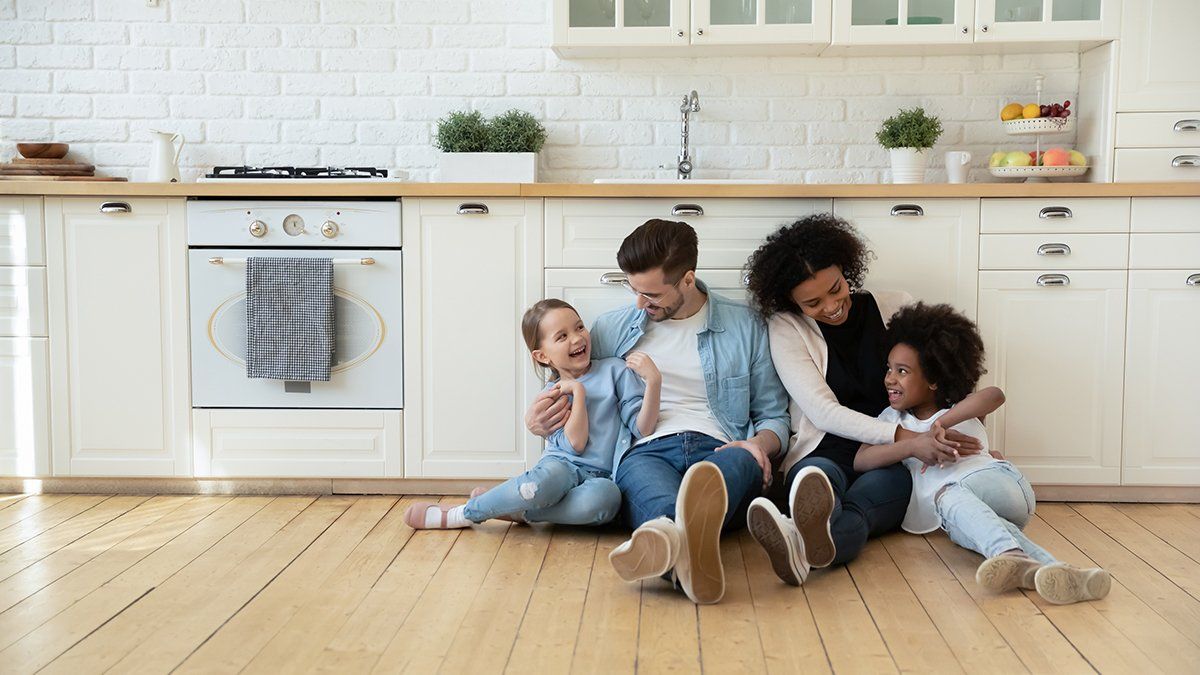 A family is sitting on the floor in a kitchen.