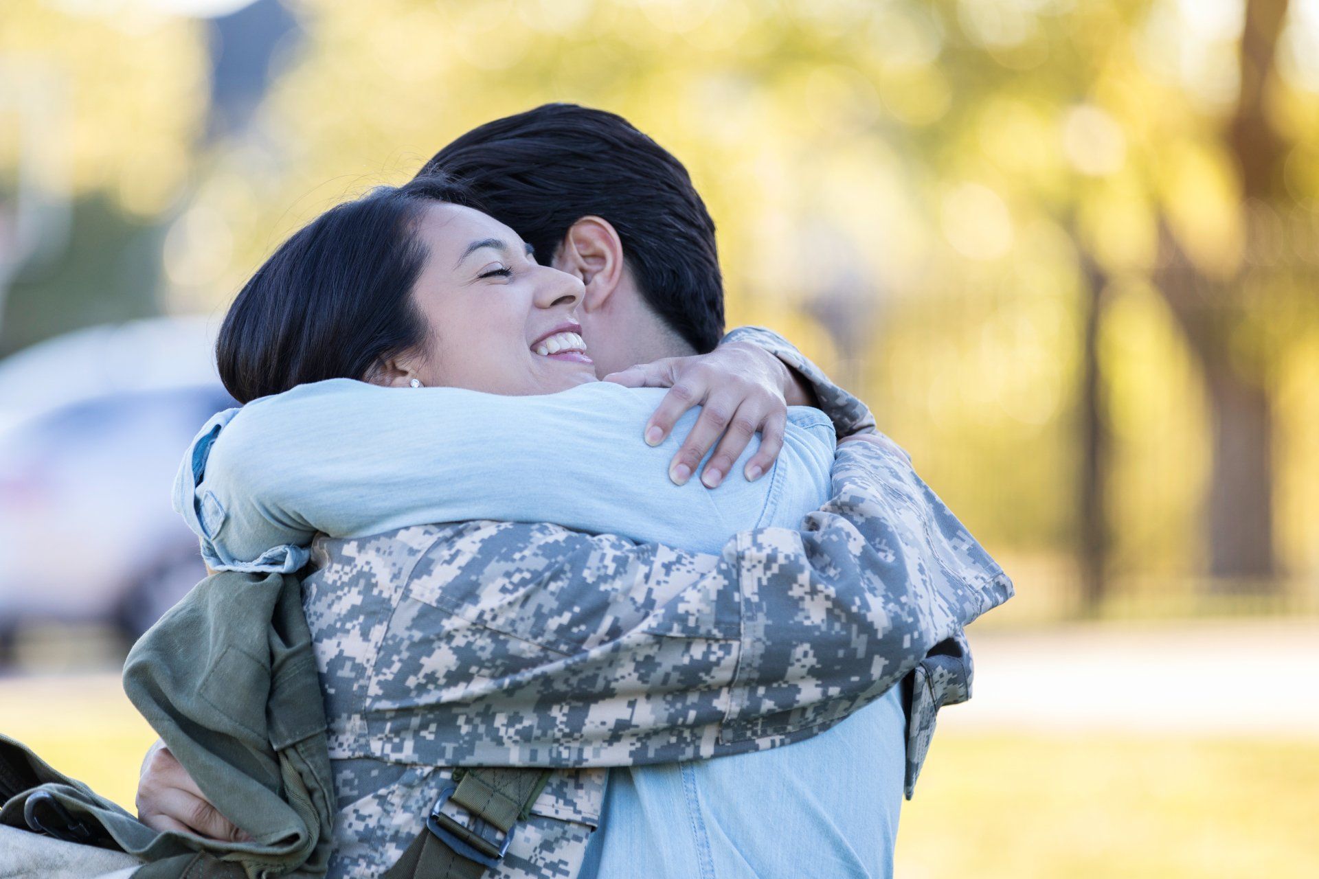 A man in a military uniform is hugging a woman in a park.