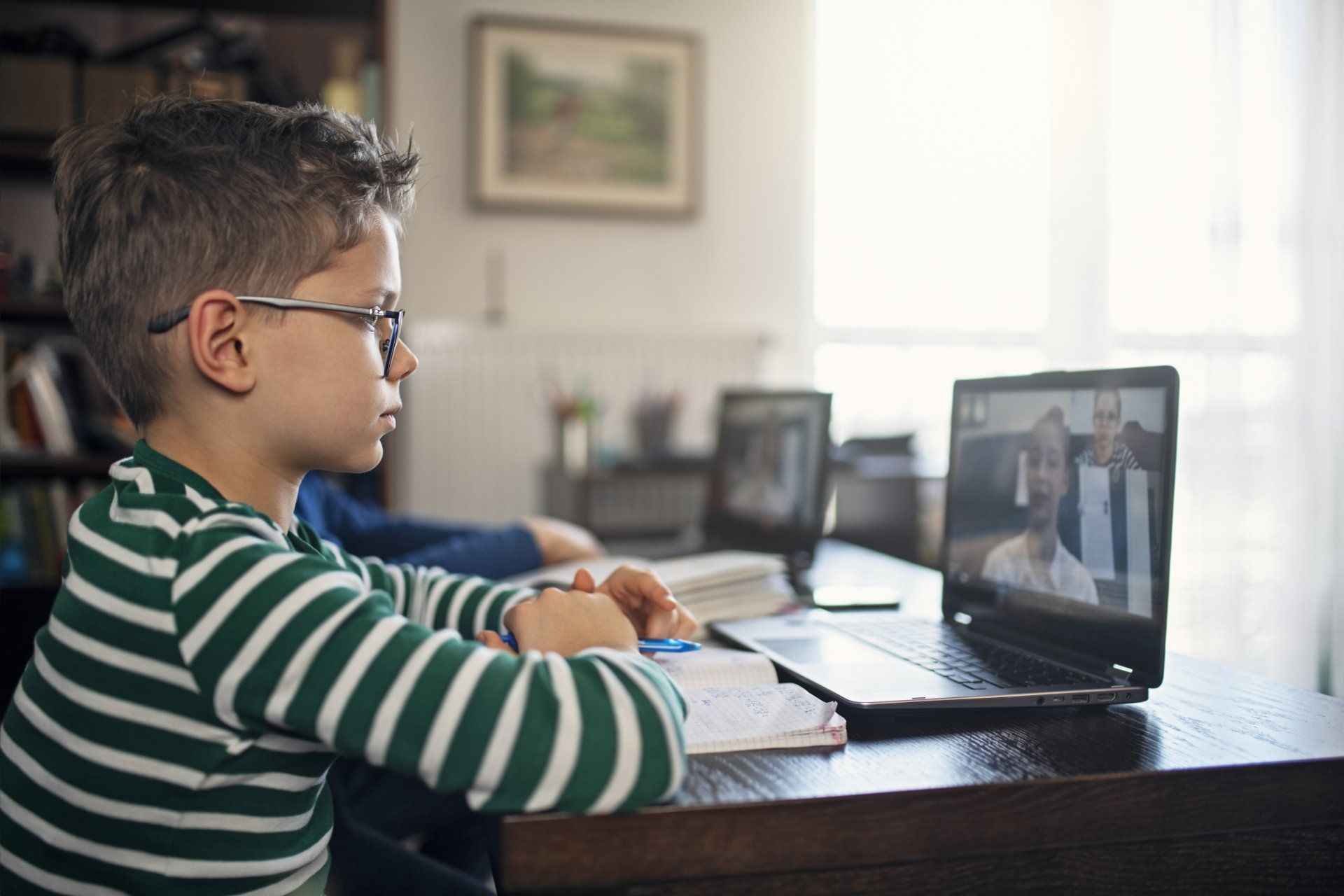 A young boy is sitting at a desk using a laptop computer.