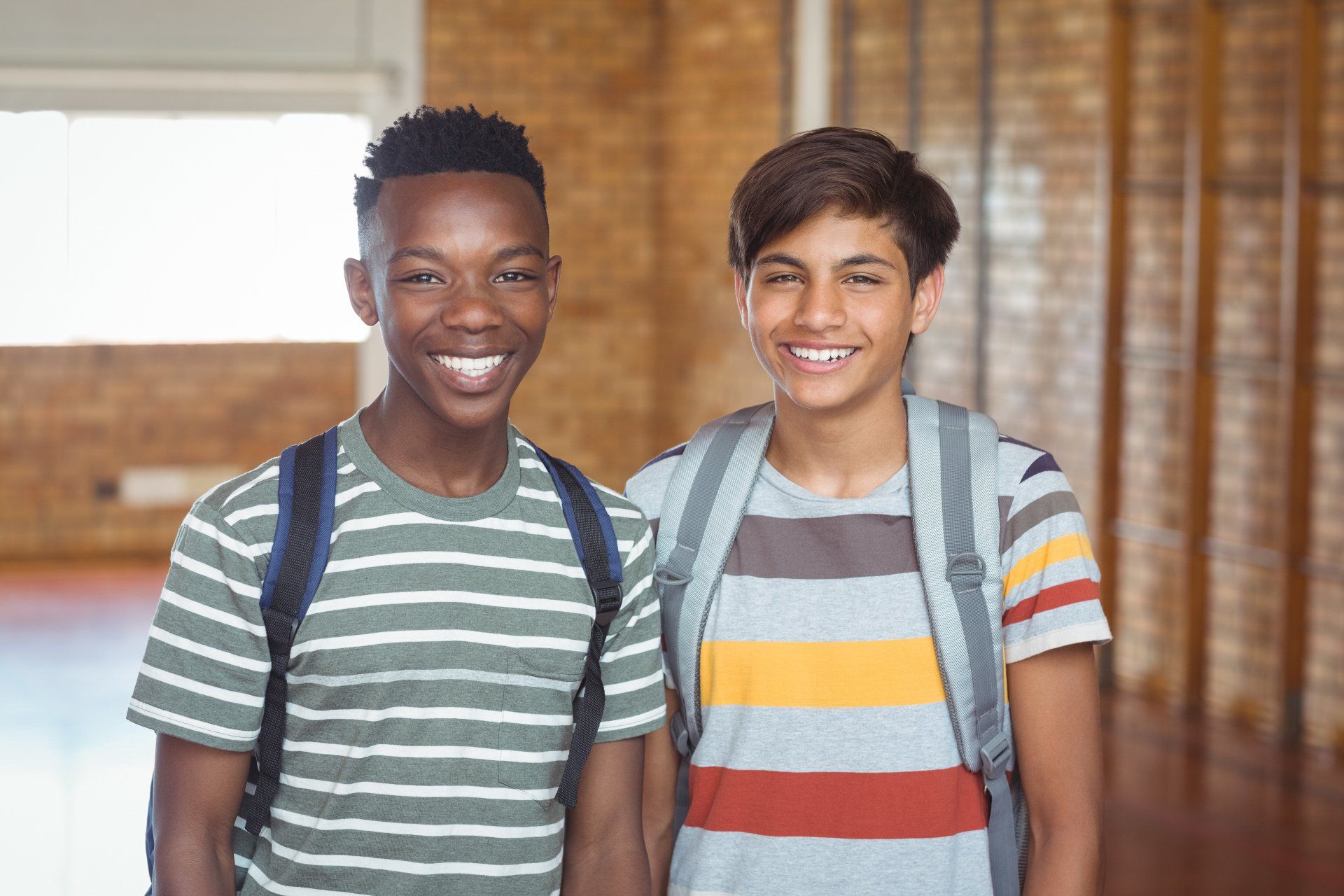 Two boys with backpacks are posing for a picture in a gym.