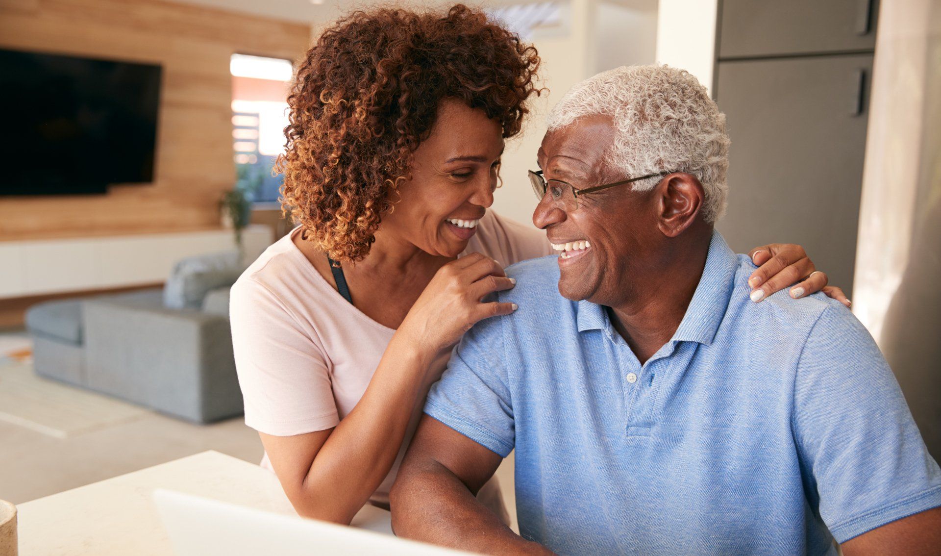 A woman is hugging an older man while sitting at a table.