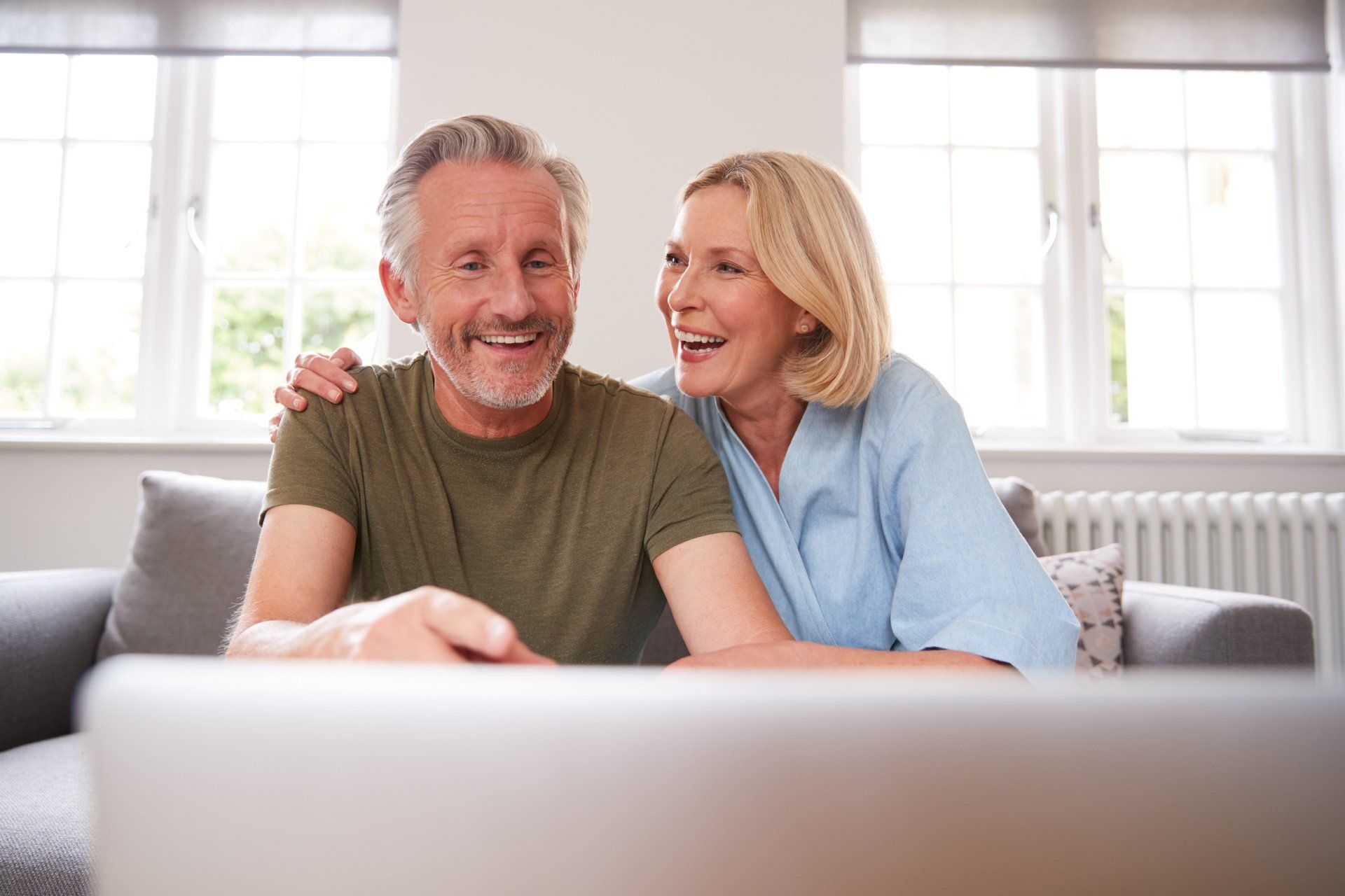 A man and a woman are sitting on a couch looking at a laptop computer.