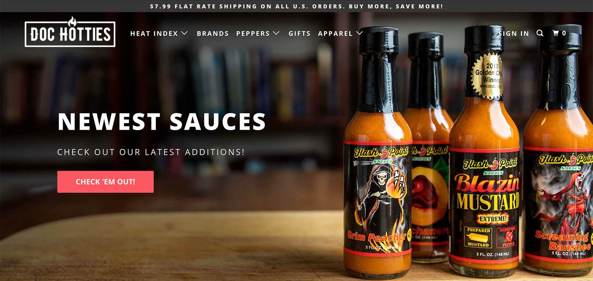 Four bottles of hot sauce are sitting on a wooden table.