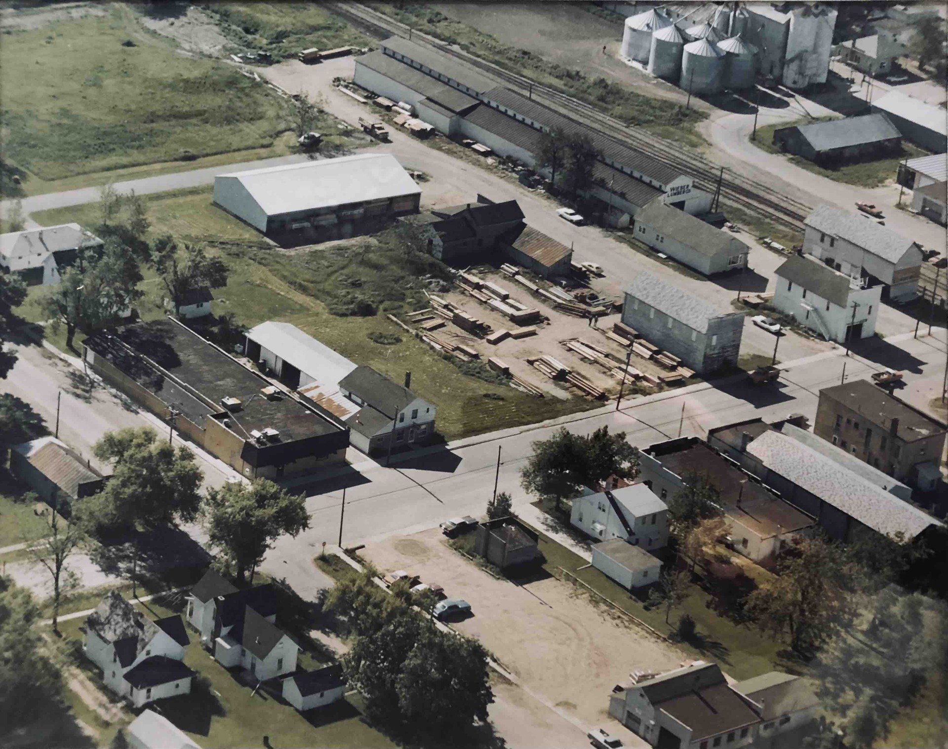 Aerial view of a small town with grain silos, a railway, various industrial warehouses, and surrounding houses.