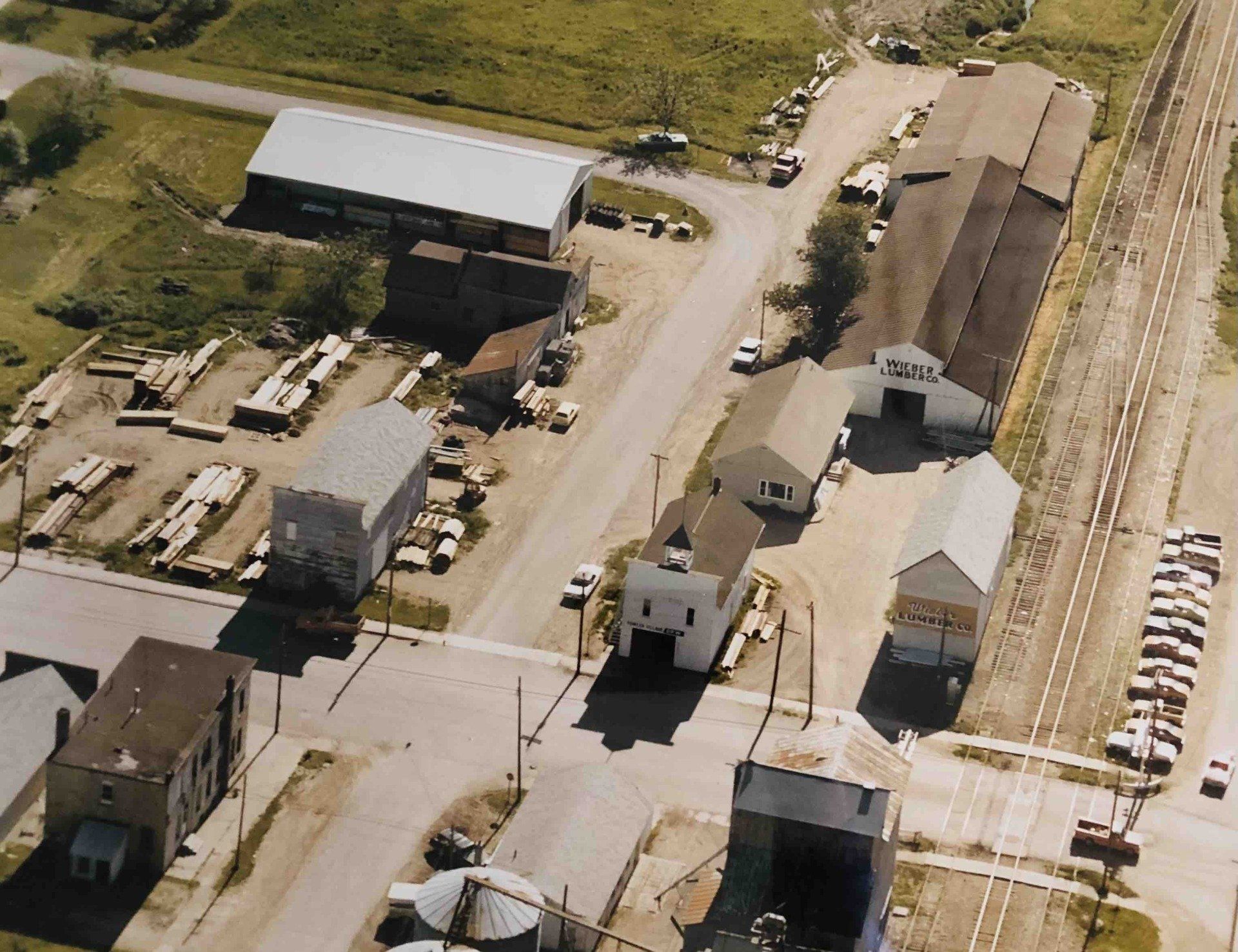 Aerial view of a small town industrial area featuring several warehouses, a lumber yard, and railroad tracks.