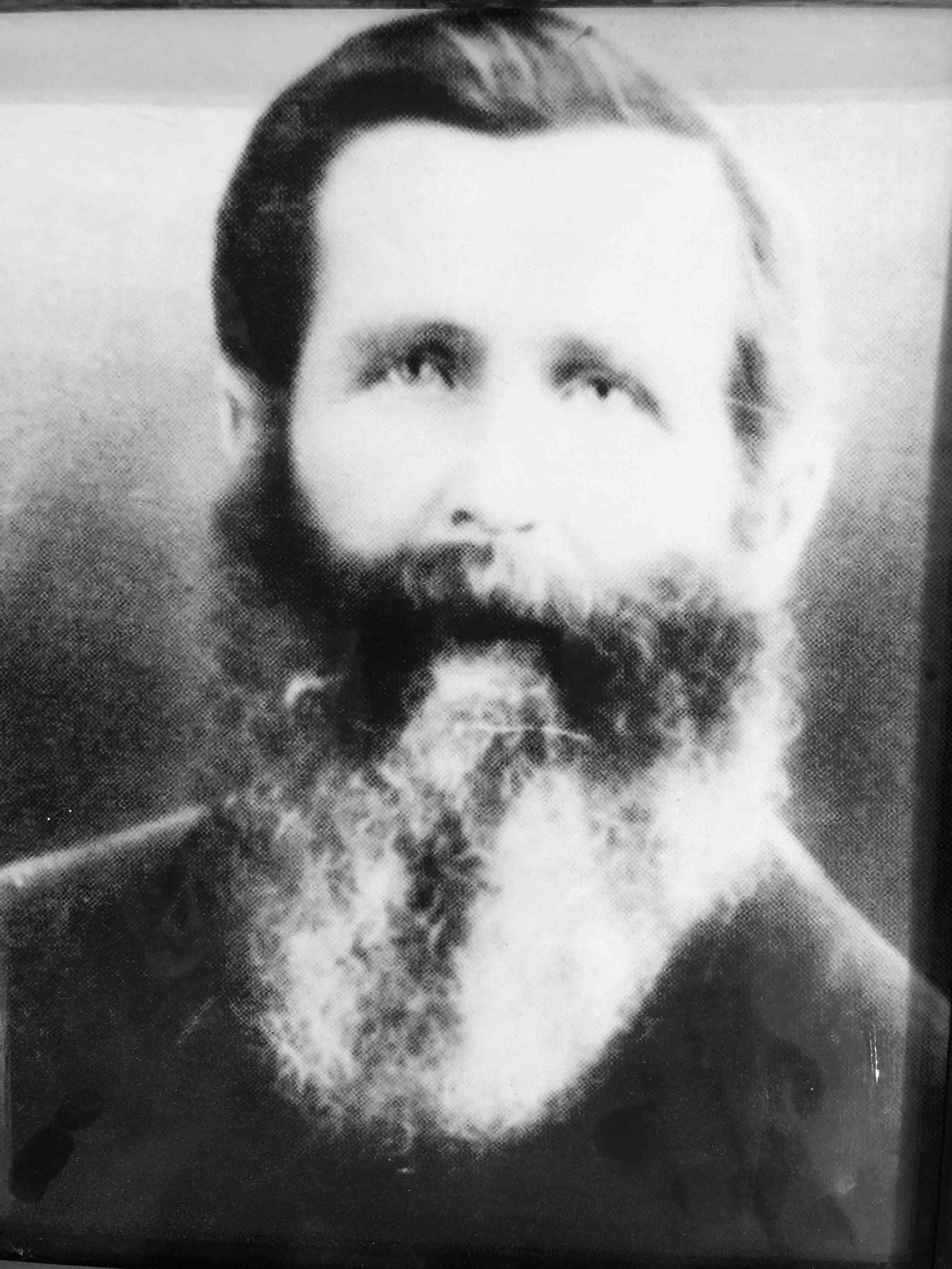 Black-and-white portrait of a person with a full, thick beard, looking directly at the camera.