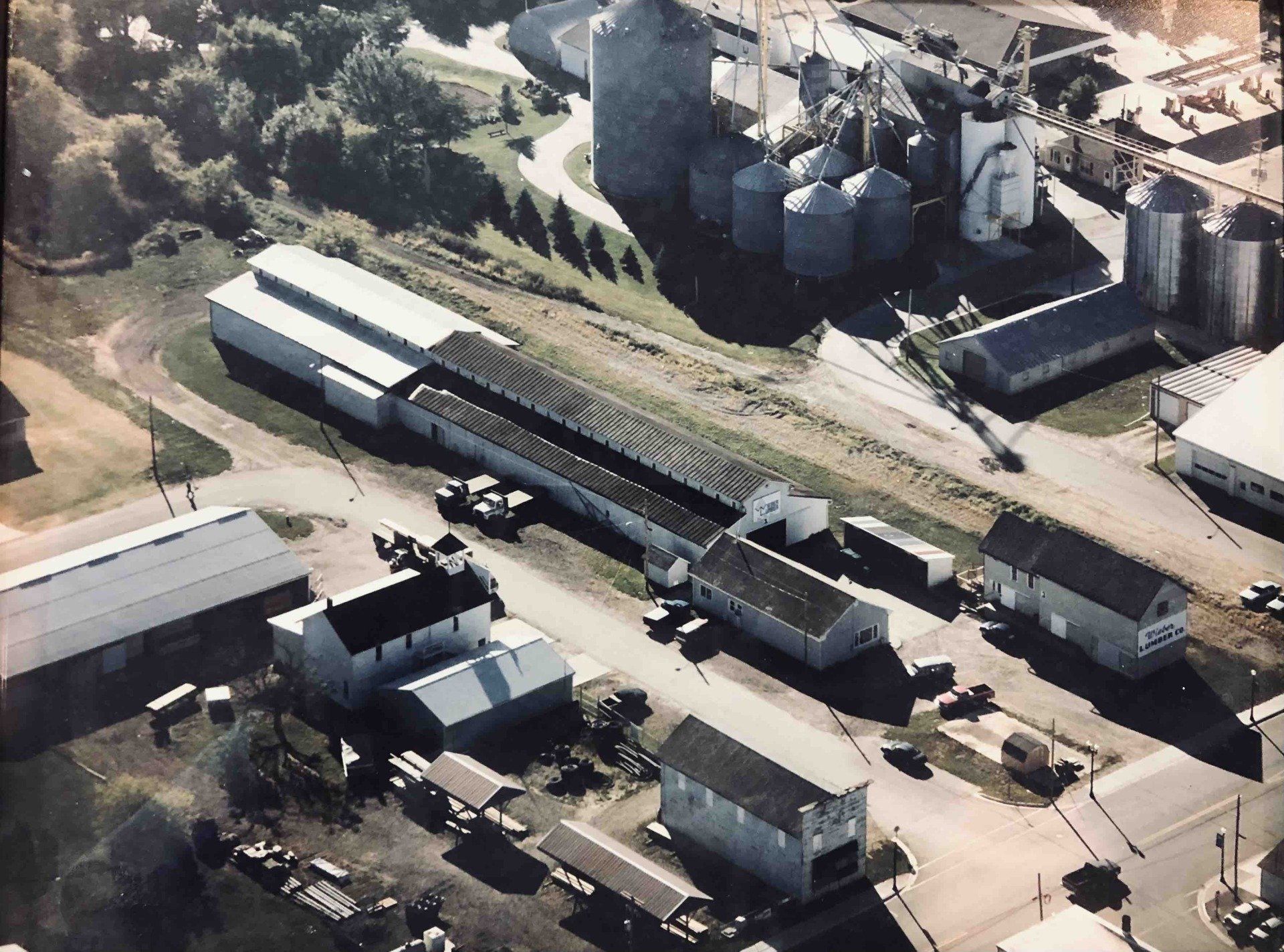 Aerial view of a rural agricultural facility with several silos, warehouses, and storage buildings.