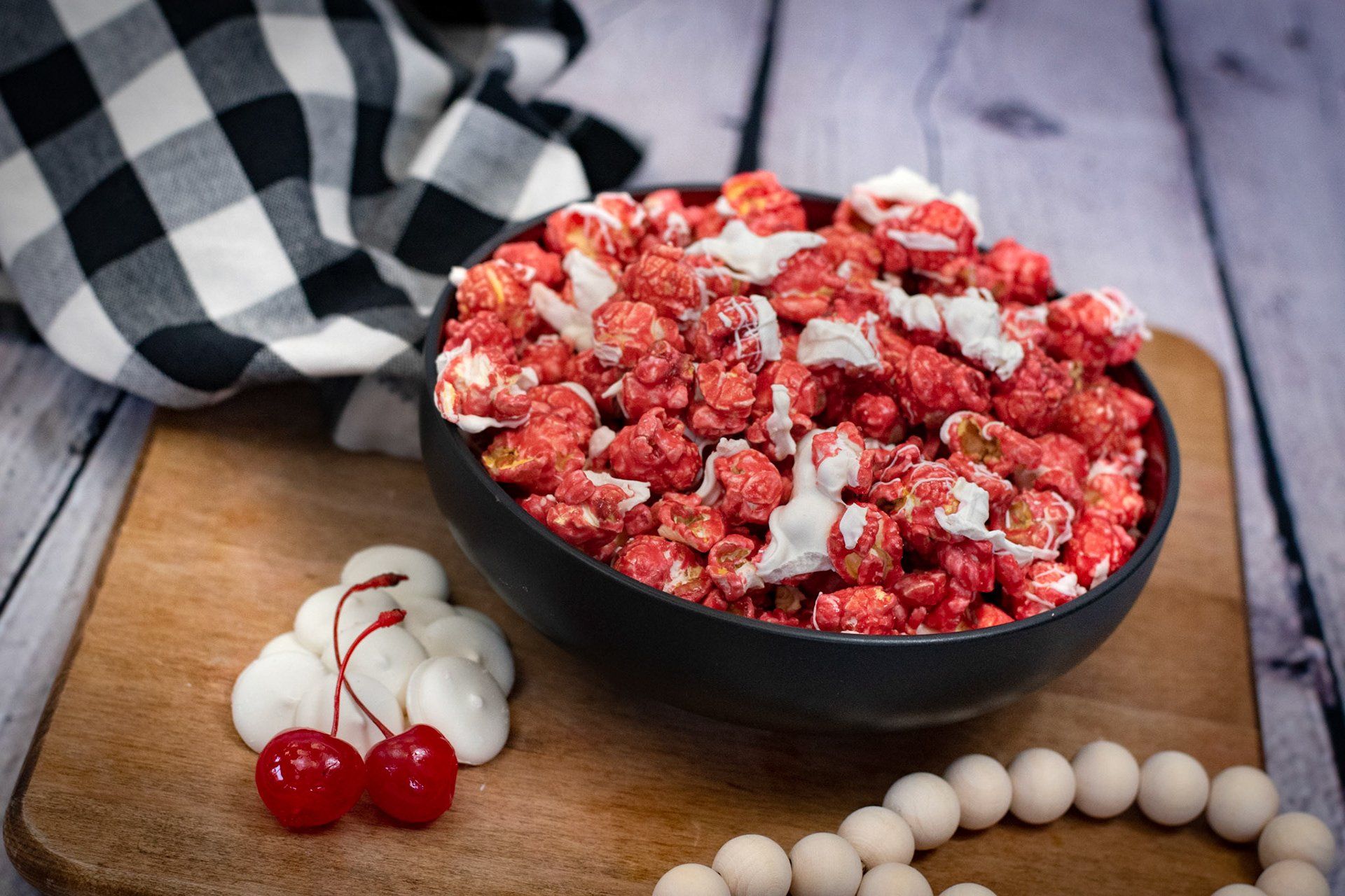 A bowl of red and white popcorn with cherries and marshmallows on a wooden table.