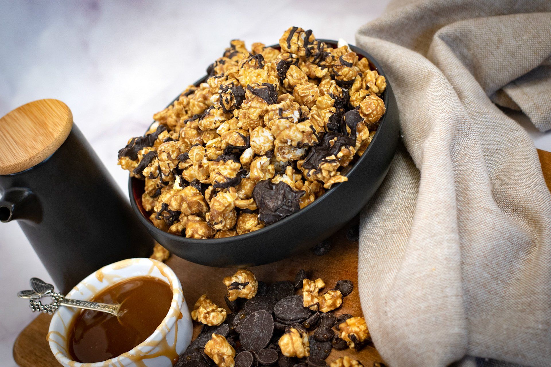 A bowl of chocolate covered popcorn next to a cup of caramel sauce.