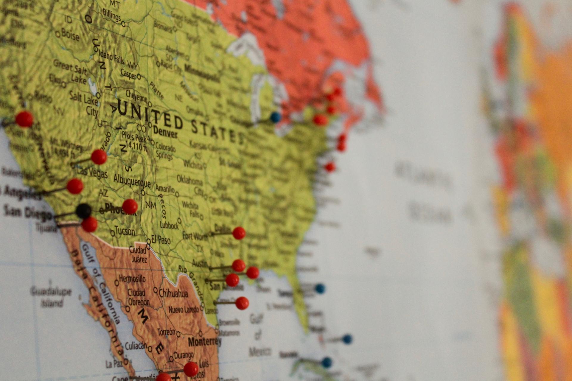 A zoomed in map of the United states lies flat on a wall with several pins on U.S. cities.