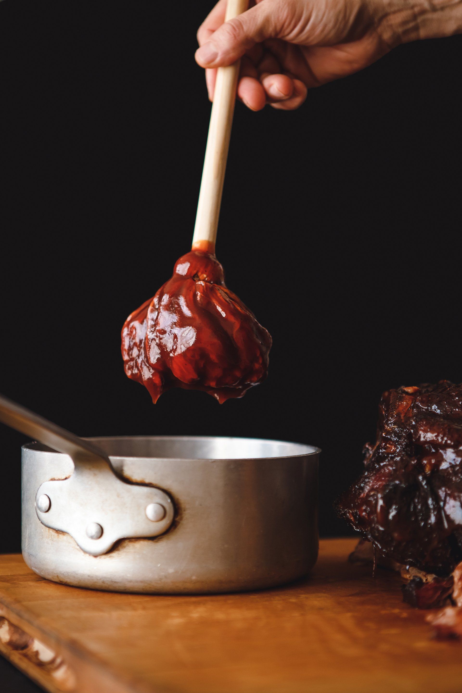A person is pouring barbecue sauce into a pot with a wooden spoon.