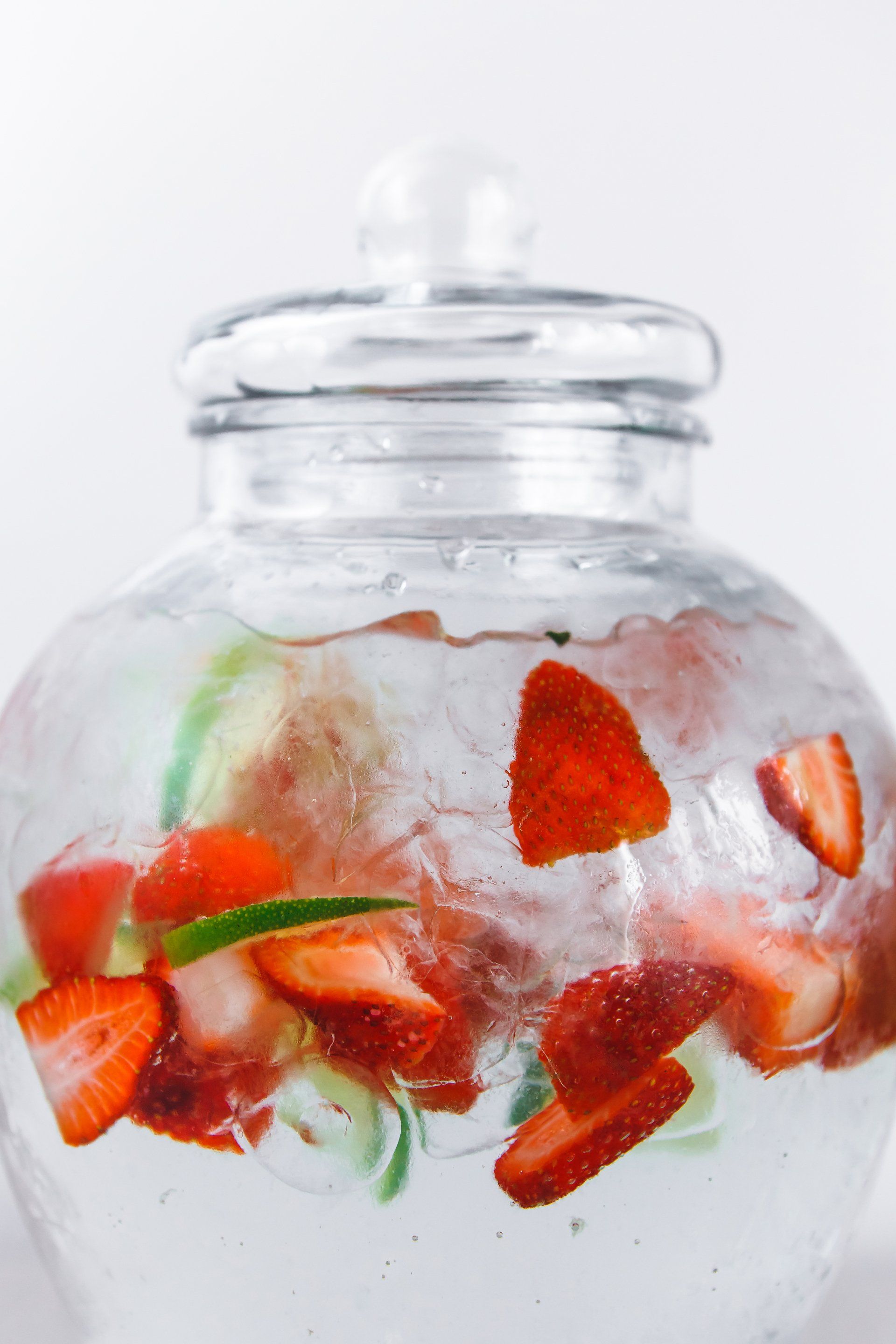 Strawberries and cucumber are in a glass jar filled with water.