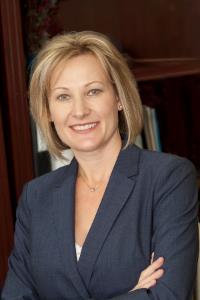A woman in a blue suit is smiling with her arms crossed.