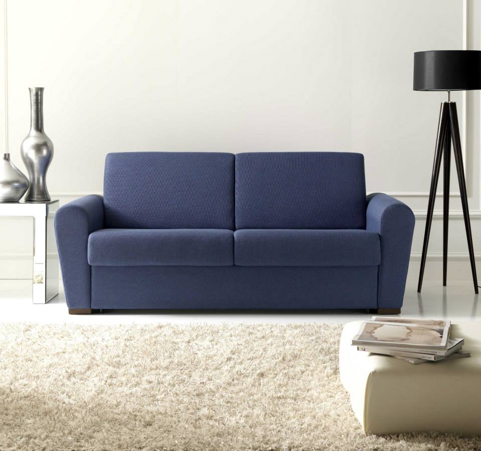 Soggiorno moderno con divano blu, lampada da terra nera, tavolino bianco e tappeto beige.