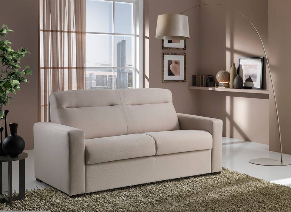 Divano beige in un soggiorno moderno con luce naturale proveniente dalla finestra, mensole a muro, lampada da terra e tappeto verde.