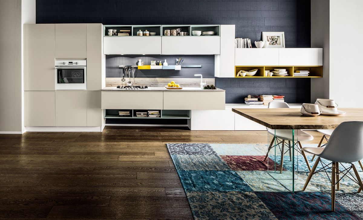 Cucina moderna a vista con mobili bianchi, pavimento in legno scuro e un tappeto colorato accanto al tavolo da pranzo.