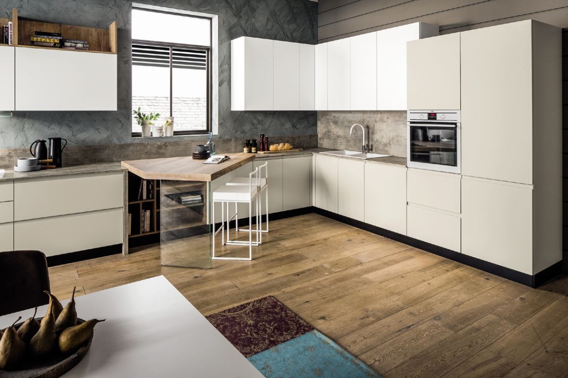 Cucina moderna bianca con ripiani in legno, forno a incasso e tavolo da pranzo accanto a una finestra.