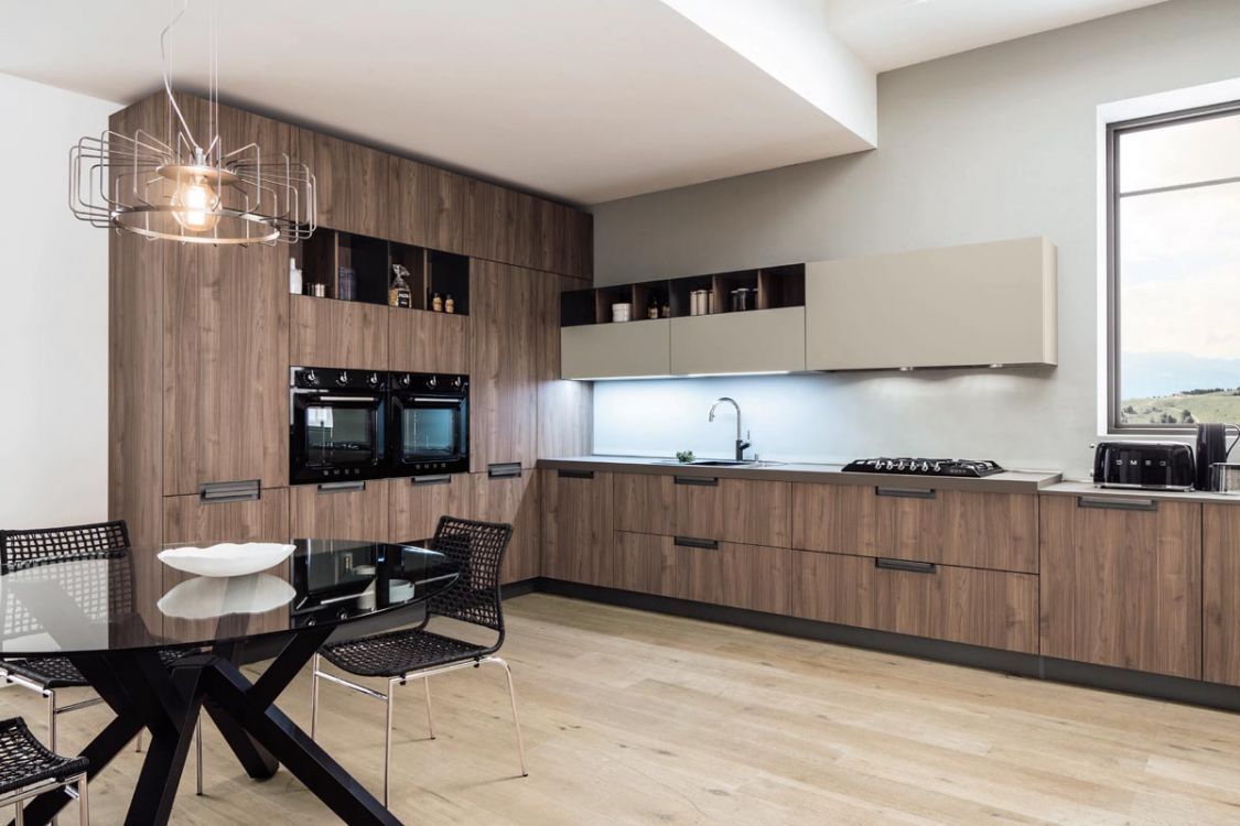 Cucina moderna con mobili in legno, tavolo da pranzo nero e ampia finestra che si affaccia su una vista luminosa