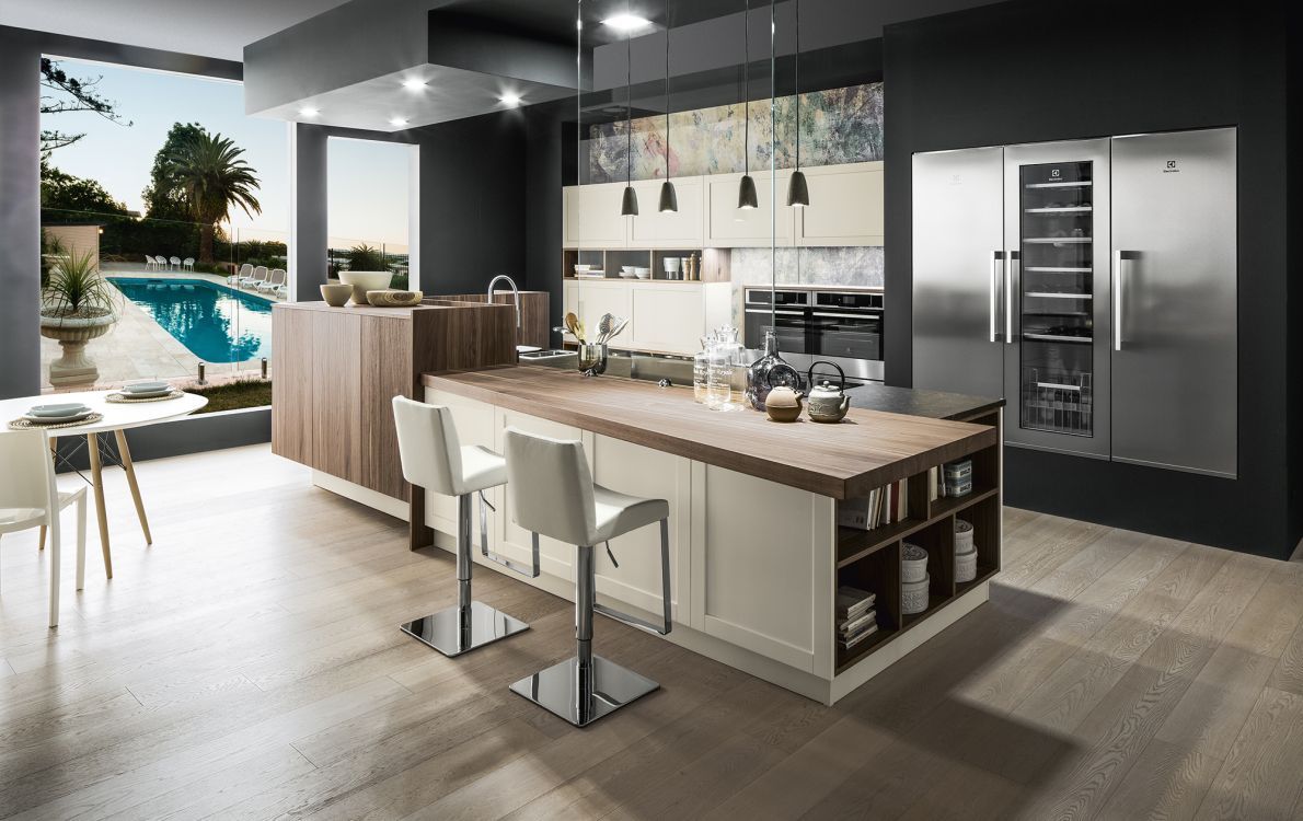 Cucina moderna a pianta aperta con isola, lampade a sospensione, frigorifero in acciaio inox e vista sulla piscina attraverso ampie finestre.