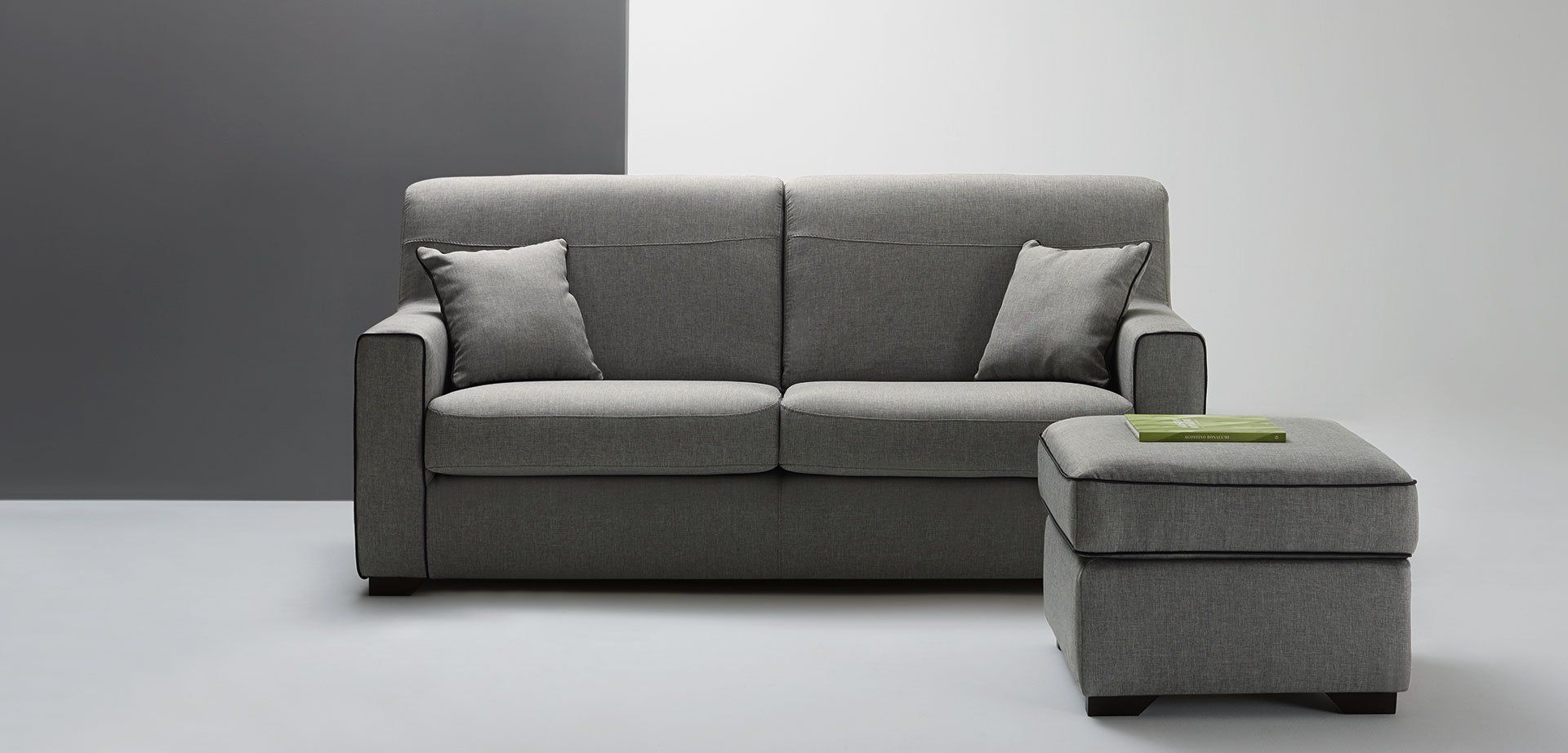 Divano grigio con cuscini e pouf abbinato su uno sfondo grigio minimalista in studio.