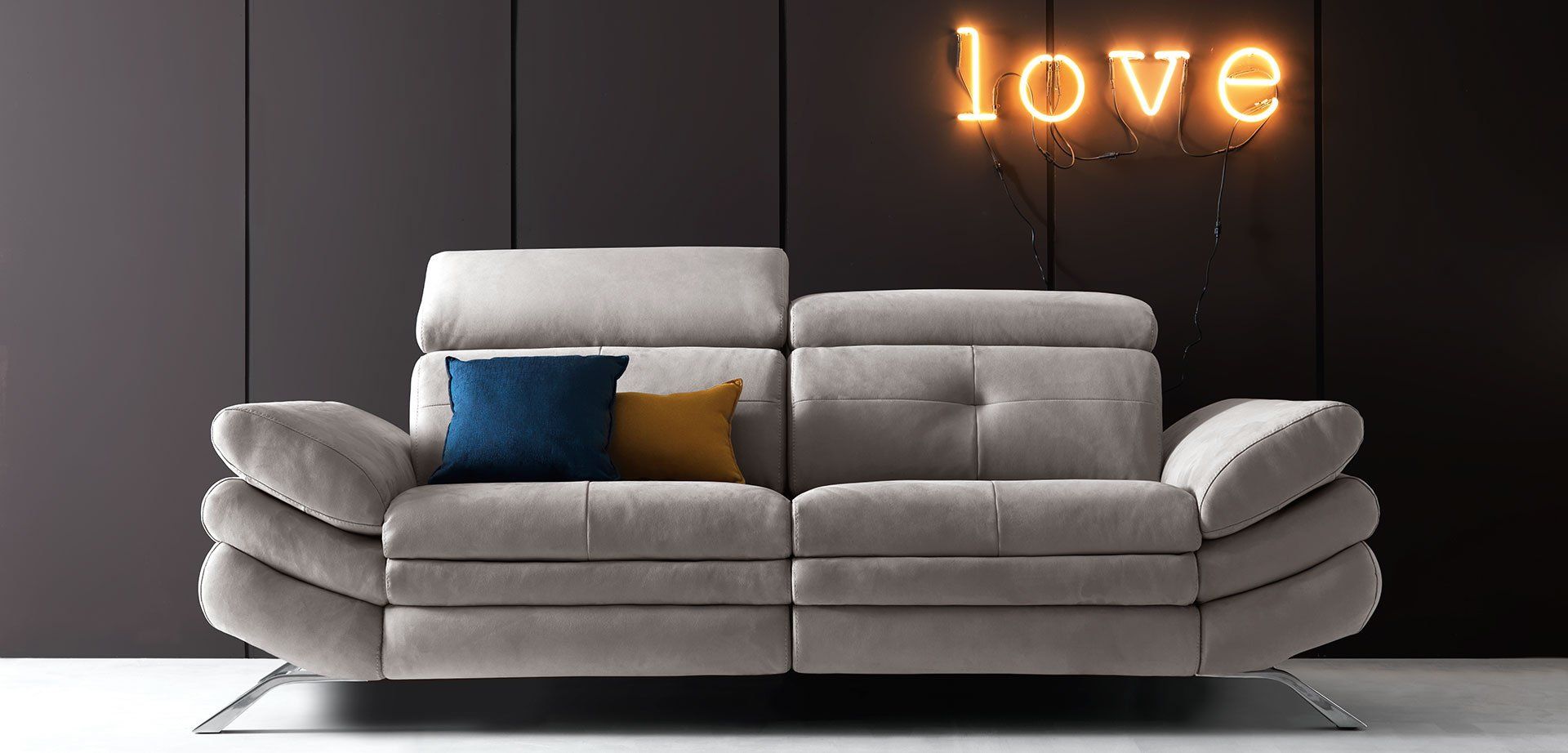 Moderno divano componibile grigio con cuscini blu e oro sotto una luminosa insegna con la scritta