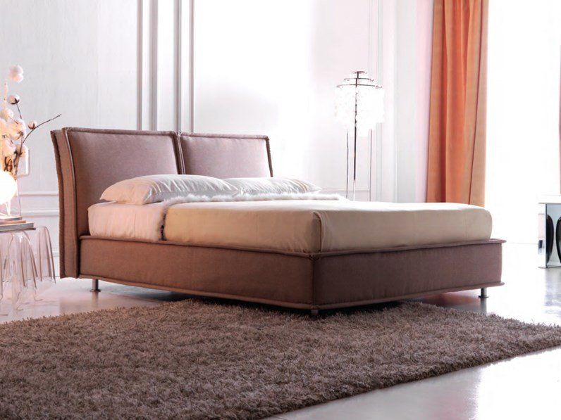 Camera da letto moderna con letto imbottito marrone su un tappeto a pelo lungo e luce naturale soffusa.
