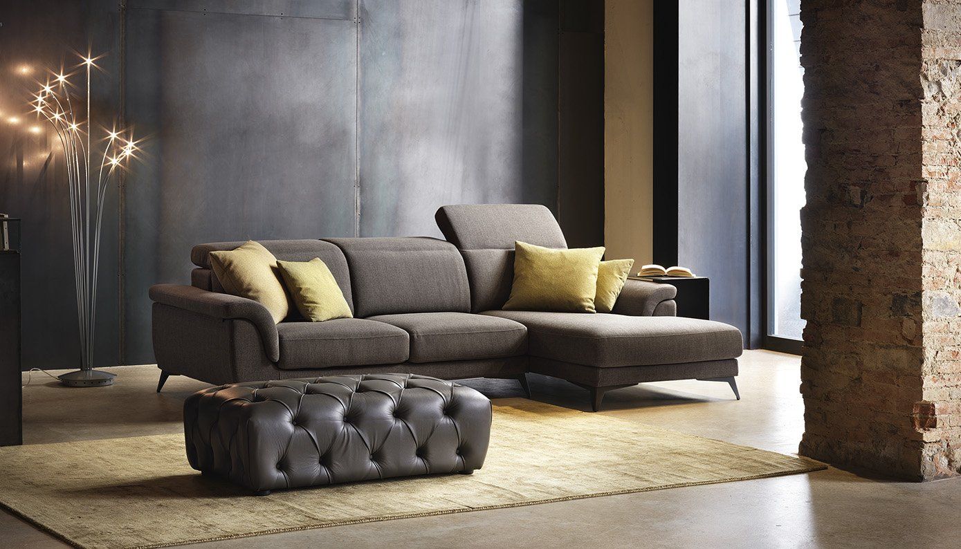 Soggiorno moderno con divano grigio, cuscini gialli, pouf e illuminazione soffusa.